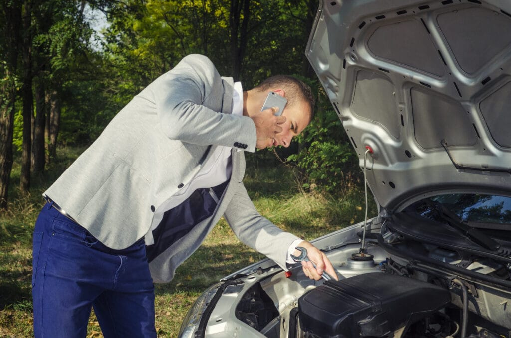 Man standing by the open hood making a phone call and trying to fix the vehicle.